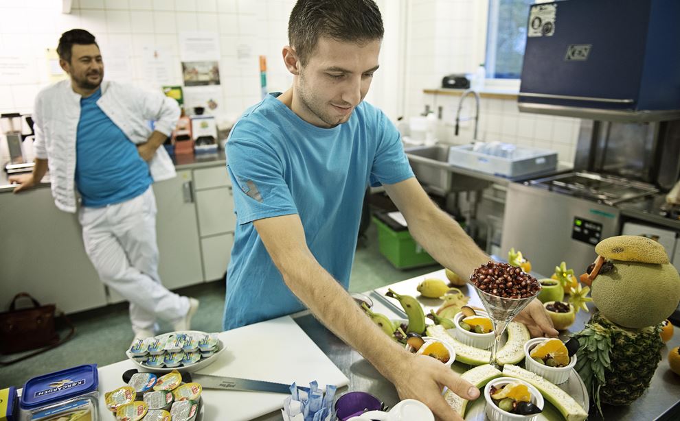 En hospitalsmedhjælper anretter frugt i et industrikøkken